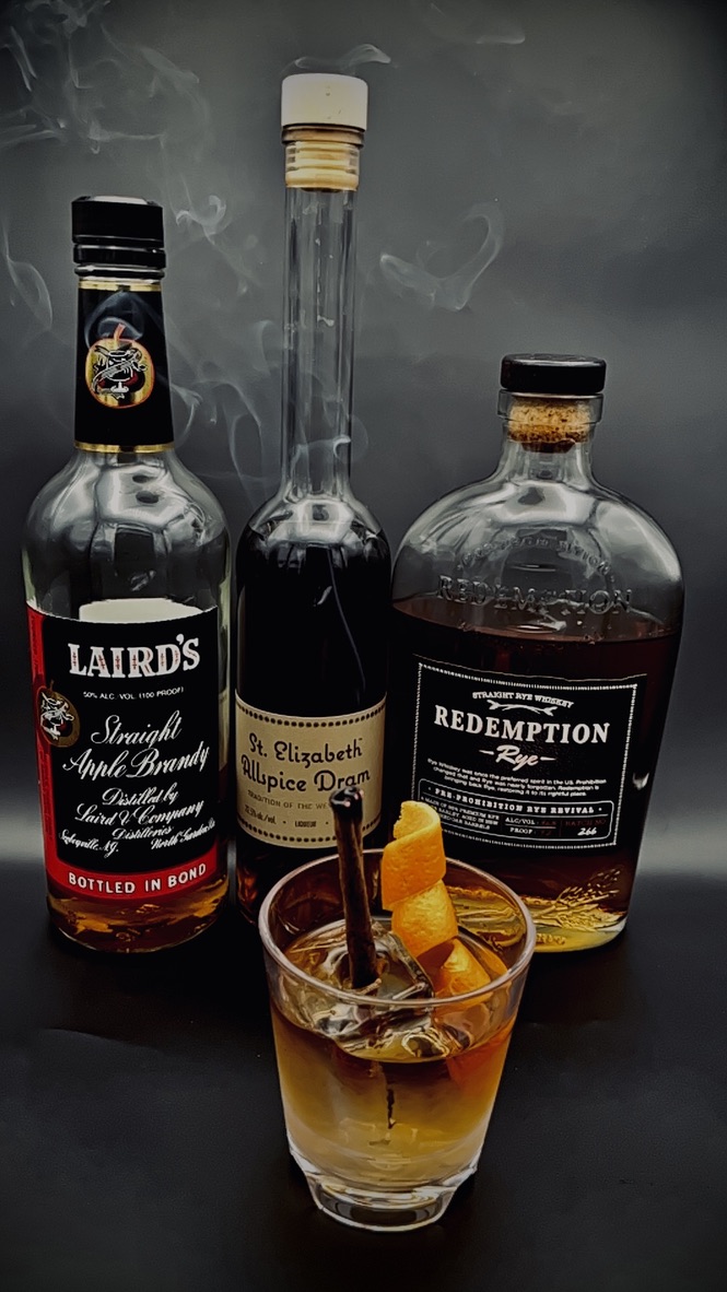 Spirit-forward cocktail with orange peel, cinnamon, and whiskey bar bottles